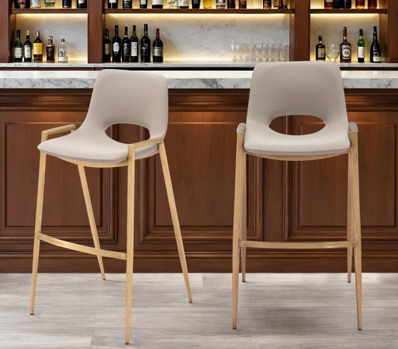 Set of two beige faux leather and steel low back bar height chairs with gold accents, ideal for home bar or counter seating.